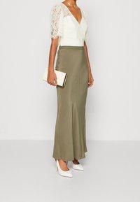 Ecru spetsblus med korta puffärmar, kombinerad med en lång olivgrön satinkjol. Vita stilettklackar och en krämfärgad kuvertväska fulländar looken.