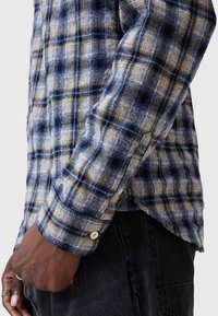 Blauw en beige geruite shirt met een textuurstof, knoopmanchetten en een getailleerd ontwerp. Close-up van de mouw en polsdetails.