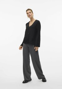Top nero texturizzato con scollo a V e maniche lunghe abbinato a pantaloni grigi a gamba larga e scarpe nere. Design semplice, vestibilità casual.
