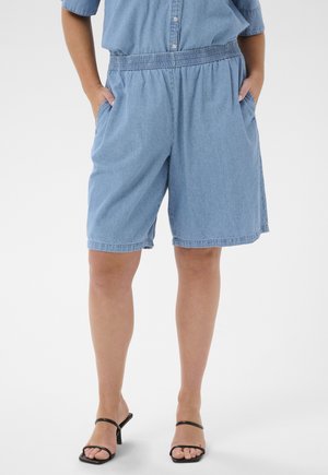 Personne portant un short en jean bleu clair avec une taille élastique et des poches latérales, assorti à des sandales noires à talons.