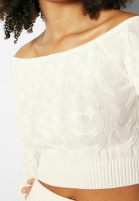 Off-the-shoulder white knit top featuring a textured pattern, ribbed hem, and cropped design for a fitted look.