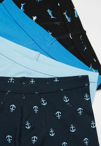 Trois paires de boxers pour hommes : bleu marine avec un motif d'ancre, noir avec un motif de requin et bleu clair uni. Tous sont en tissu coton extensible.