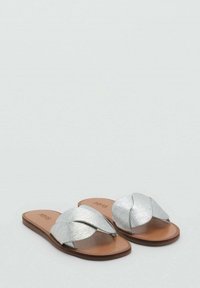 Sandali in metallo argentato con un design annodato su una soletta color beige, con suola piatta e senza tacco.