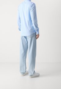 Camisa azul claro abotonada con mangas largas, combinada con jeans de corte holgado azul claro y zapatillas blancas. Textura de tela suave, diseño casual.