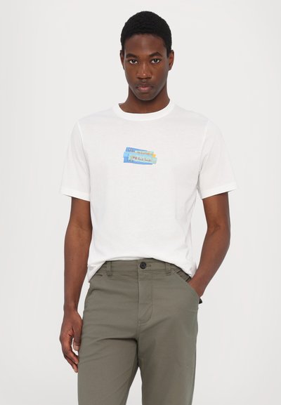 T-shirt en coton blanc à manches courtes et col rond, avec un design coloré imprimé sur la poitrine, associé à un pantalon vert olive.