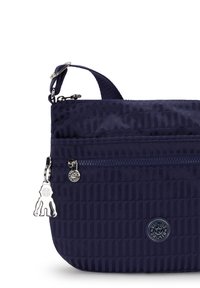 Borsa in nylon blu navy con un design testurizzato, hardware della cerniera in argento e un charm in metallo. Presenta una tasca anteriore con cerniera e una tracolla regolabile.