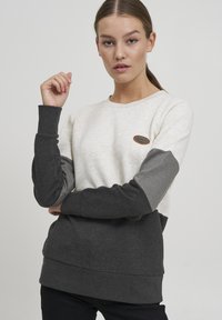 Vaaleanharmaa ja tummanharmaa väriestoitettu collegepaita pitkillä hihoilla, pyöreällä kaula-aukolla ja pienellä logopatchilla rinnassa. Pehmeä pinta.
