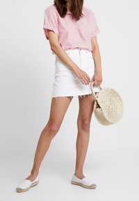 Bílá denimová minisukně s roztrhaným lemem, v kombinaci s růžovou a bílou pruhovanou košilí s krátkým rukávem a bílými espadrilkami. Tkaný slaměný sáček.