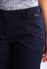 Marina blå byxor med en slät yta, hållbart tyg, en framficka och en märkesetikett nära midjan. Knappt stängning vid midjan.