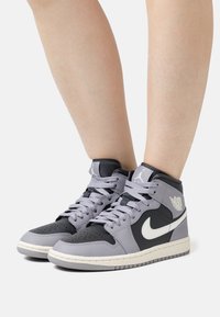 Wysokie trampki z czarno-szarym skórzanym wierzchem. Wśród cech znajdziemy perforowany czubek buta, szare sznurówki i białe logo Nike Swoosh.