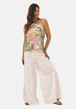 Top halter de tela verde con estampado floral, combinado con pantalones anchos de pierna ancha en color blanco y con volantes. Acentuado con un borde de encaje y sandalias doradas.