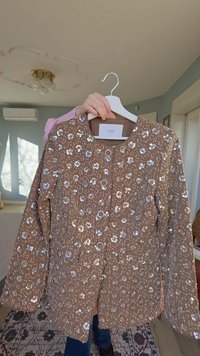 Giacca marrone con motivo floreale a paillettes, scollo rotondo, chiusura con bottoni e tessuto strutturato. Maniche lunghe con cuciture dettagliate.