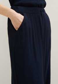 Námořnické sklady s kapsami po stranách a strukturovanou tkaninou. Pas je dobře padnoucí, což zvyšuje pohodlí a funkčnost.