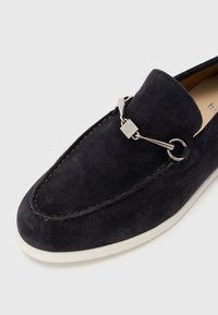 Tumesinine sametist loafers valge tallaga, dekoratiivne hõbedane riistvara ja kontrastne õmblus ääres. Sile tekstuur, klassikaline disain.