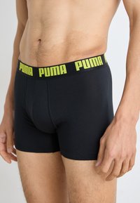 Boxeri negri din bumbac, cu un design ajustat, având o talie elastică lată de culoare verde neon, cu logo-ul "PUMA" afisat proeminent.
