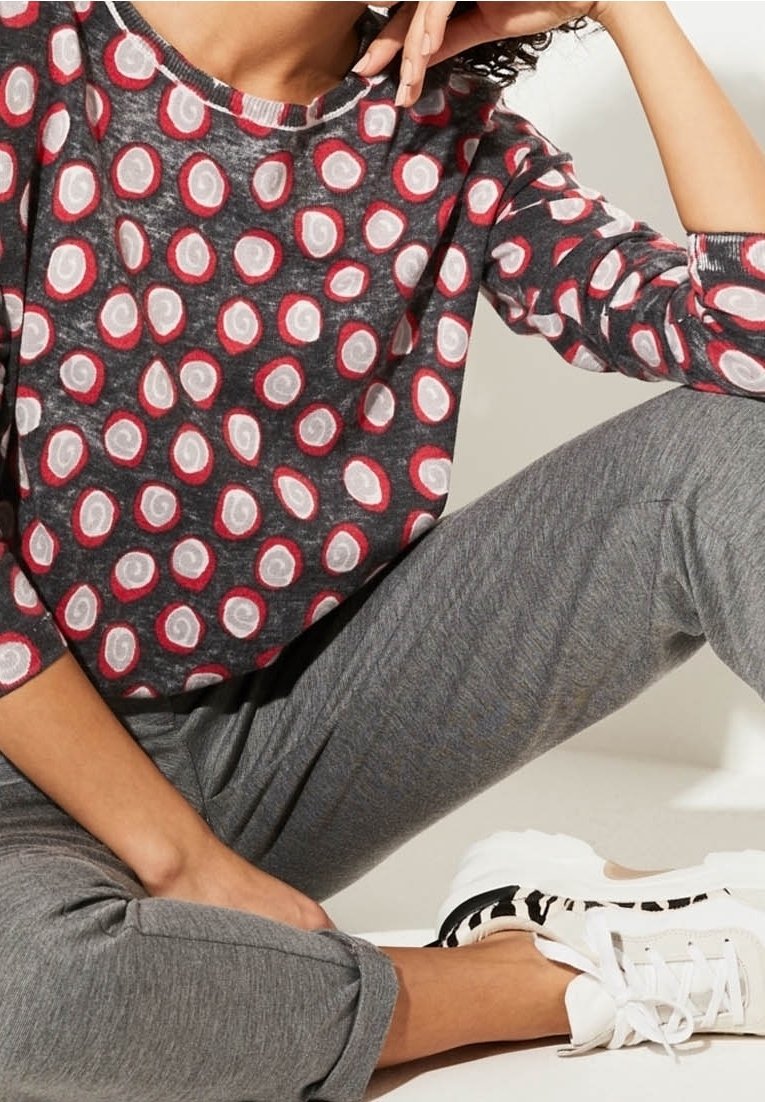 Graues Langarmshirt mit roten und weißen Wirbelmustern, kombiniert mit grauen Hosen und weißen Sneakers mit schwarzen Akzenten.