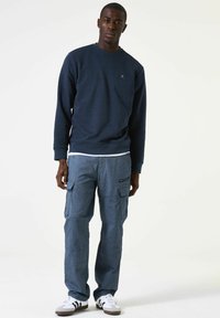 Marine sweatshirt met gestructureerd ontwerp, ronde hals en geribbelde boorden, gecombineerd met lichtblauwe cargobroeken met zijzakken en een losse pasvorm. Witte sneakers.