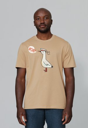 Beige T-shirt met korte mouwen, met een cartoonvogel met een hoed en de tekst "MOIN!" in een spraakbubble. Zachte stof, eenvoudig ontwerp.