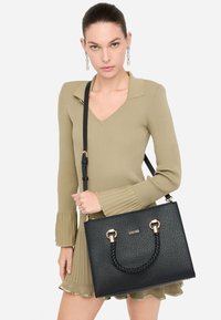 Sort struktureret håndtaske med vævet toprem og guldfarvede metaldele. Teksturmateriale med en aftagelig skulderrem.