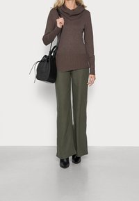 Brązowy sweter z kołnierzem typu cowl, z prążkowanym dołem, w połączeniu z oliwkowymi spodniami z szerokimi nogawkami i czarnymi botkami do kostki. Czarna pleciona torba typu bucket jako akcent.