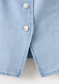 Tissu en denim bleu clair avec deux boutons-pression argentés et un ourlet fendu à l'avant, présentant une couture détaillée sur les bords du vêtement.