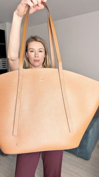 Stor tan läder tote väska med texturerad yta, långa handtag och subtila sömdetaljer. Väskan hålls upprätt mot en neutral bakgrund.