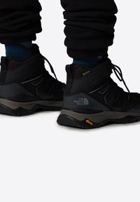 Czarne buty trekkingowe z teksturowanymi powierzchniami, wysoką cholewką i podeszwą Vibram, posiadające oznaczenia marki oraz akcenty GORE-TEX zapewniające wodoodporność.
