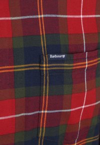 Rood, groen en marineblauw geruit stof met een textuurweefsel. Bevat een zak met een blauwe Barbour-label. Accenten in wit en geel.