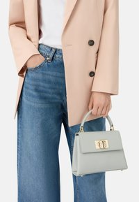 Grijze gestructureerde handtas met een bovenste handvat, goudkleurige hardware en een sluiting met gesp, gecombineerd met een lichtroze blazer en blauwe spijkerbroek.