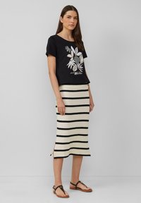 Zwarte korte mouwen shirt met een bladerenafbeelding en tekst, gecombineerd met een gestreepte crème en zwarte gebreide rok. Bevat zijsplitten en platte sandalen.