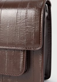 Geantă maro din piele cu finisaj lucios, prevăzută cu dungi verticale și margini cusute. Clapă pliabilă cu închidere magnetică.