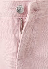 Material denim roz deschis cu textură vizibilă, un nasture argintiu și detaliu cu fermoar la braguță. Sunt prezente și cusături cusute.