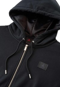 Sudadera negra con cremallera, de textura suave, con capucha forrada, cremallera plateada y un parche con el logo de Jordan en el pecho.
