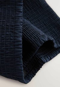 Tmavomodrá texturovaná tkanina so záhybmi, zobrazujúca hladký, pružný povrch a rôzne vzory stehov, zrolovaná na okraji.