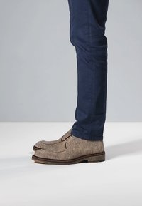 Braune Filzstiefel mit abgerundetem Zehenbereich und dekorativen Nähten, kombiniert mit marineblauen Slim-Fit-Hosen. Sichtbare unifarbene, strukturierte Materialien.