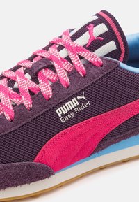 Fialové tenisky s růžovými akcenty, strukturovaná látka a vzorované tkaničky. Obsahují značku Puma a retro design. Lehká podrážka.