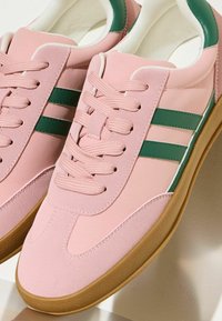 Rozā sporta apavi ar zaļām svītrām, gluds un teksturēts augšdaļa, apaļa purngala daļa, plakanā gumijas zole un teksturēta gumijas zole, kas nodrošina saķeri.