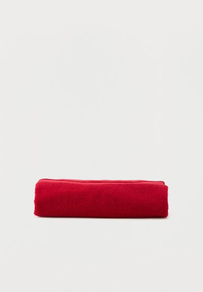 Rødt frottéhåndklæde pænt foldet på en enkel hvid overflade.