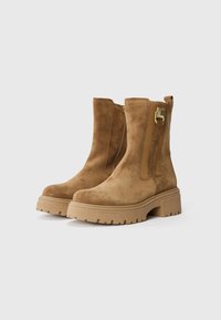 Botas de tobillo de ante marrón con suela gruesa, cremallera lateral y un pequeño acento dorado. Presenta una textura suave y una suela robusta para mayor tracción.