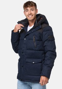 Marineblå quilted jakke med en sort skuldersektion, aftagelig hætte, to frontlommer og en lynlås brystlomme, med tekstureret stof.