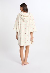 Poncho asciugamano con cappuccio di colore crema, decorato con piccoli motivi a forma di cuore rosa. Realizzato in morbido materiale peluche. Fit morbido con maniche ampie.