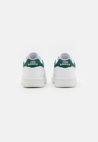Vita sneakers med en grön hälaccent och "New Balance"-logotyp. Slät läderöverdel, tjock gummisula och snörning.