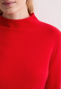 Czerwony sweter z wysokim kołnierzem, wykonany z miękkiego materiału, charakteryzujący się gładką teksturą i dopasowanym krojem. Brak widocznych wzorów lub akcentów.