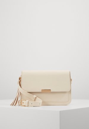 Crèmekleurige crossbodytas van glad leer, voorzien van een klep met sluiting, goudkleurige hardware en een decoratieve kwast aan het hengsel.