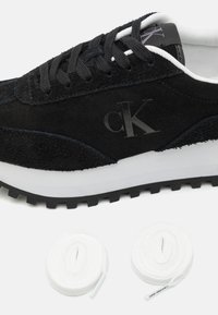 Sneaker in suede nero con accenti bianchi, lacci neri tondi e suola texture. Include due paia di lacci bianchi aggiuntivi.