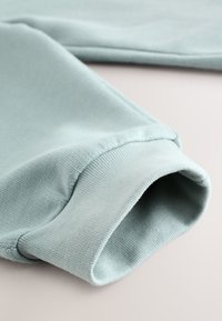 Manche de sweat-shirt bleu clair avec poignets côtelés, présentant une texture lisse et une coupe décontractée. Le matériau semble doux et extensible.