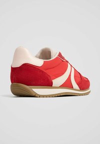 Chaussures de sport rouges et crème avec des accents en daim, une semelle en caoutchouc et un col rembourré. Présentent des lignes courbes et un design texturé.
