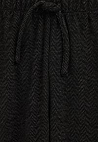 Melnas herringbone raksta bikses ar teksturētu audumu, kurām ir elastīga josta un aukla regulējamai pielāgošanai.