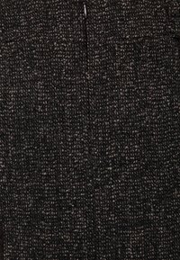 Tela negra texturizada con un patrón tejido que presenta motas gris claro y un detalle visible de cremallera en el centro.