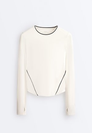 Bela majica z dolgimi rokavi, črnim obrobami na ovratniku in straneh, z manšetami z luknjami za palce in rahlo ukrivljenim robom.